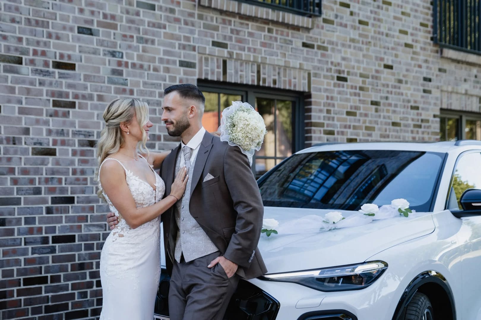 brautpaar lehnt am hochzeitsauto blumenschmuck brautstrauss
